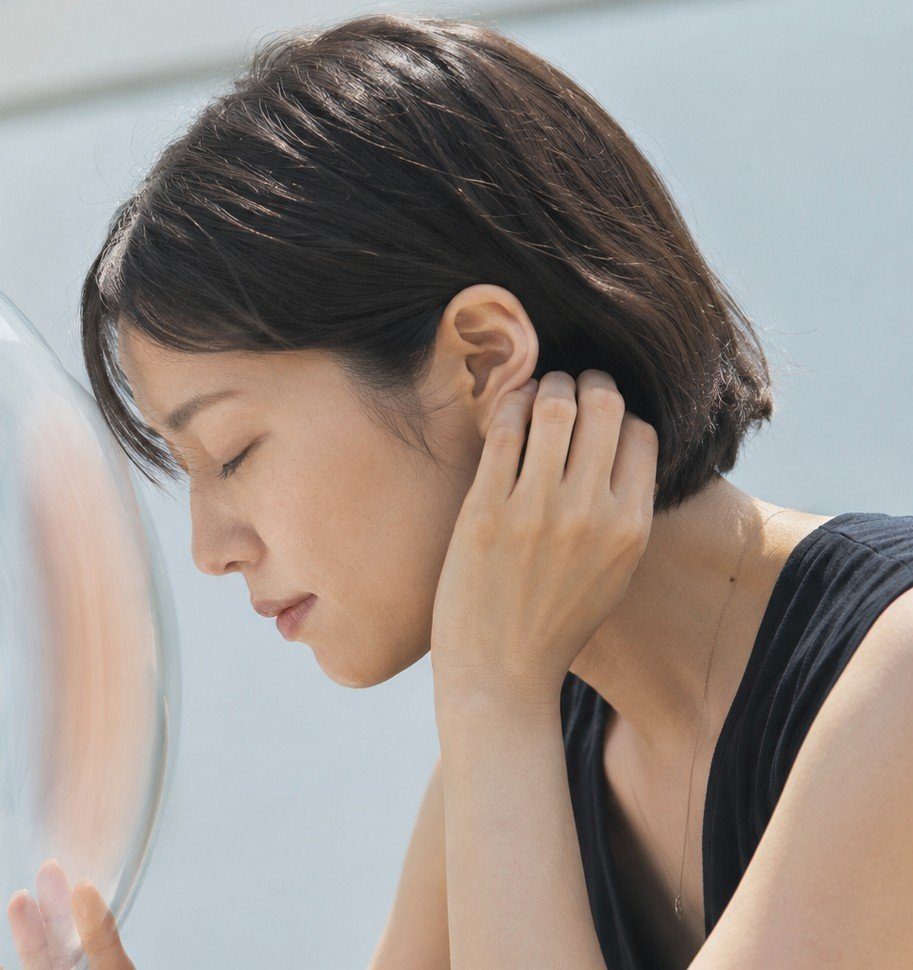 A serene woman with short brown hair and closed eyes leans against a clear surface, wearing a black top.