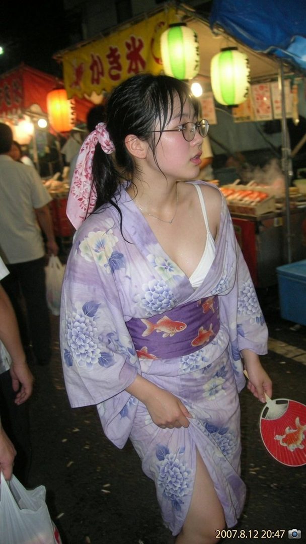 Young woman in a purple floral yukata walking at a nighttime Japanese festival with lanterns and food stalls.
