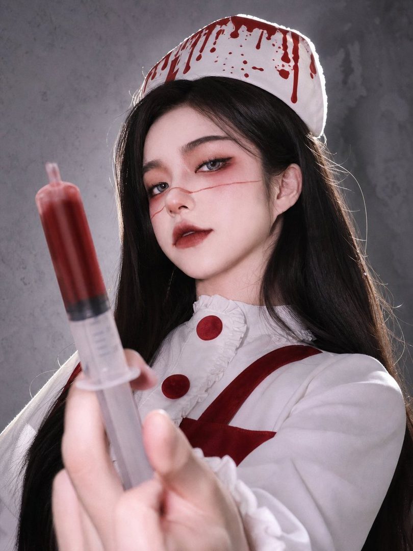 A woman dressed as a dark nurse with a blood-splattered hat and a large syringe filled with red liquid.