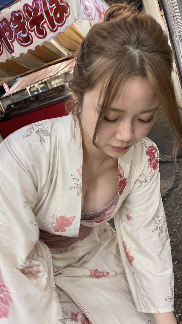 A woman in a yukata with a deep neckline is looking down on a street at night.