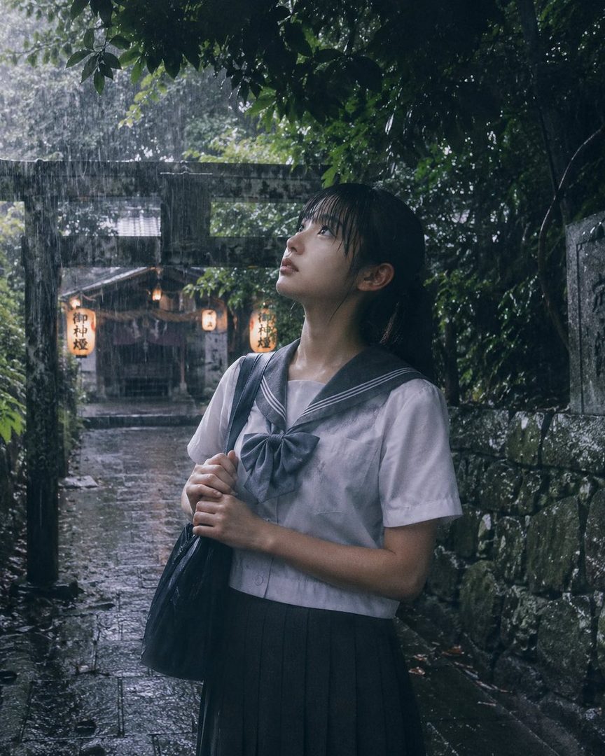A young woman in a Japanese school uniform stands in the rain, looking up, with a traditional torii gate and lanterns in the background.