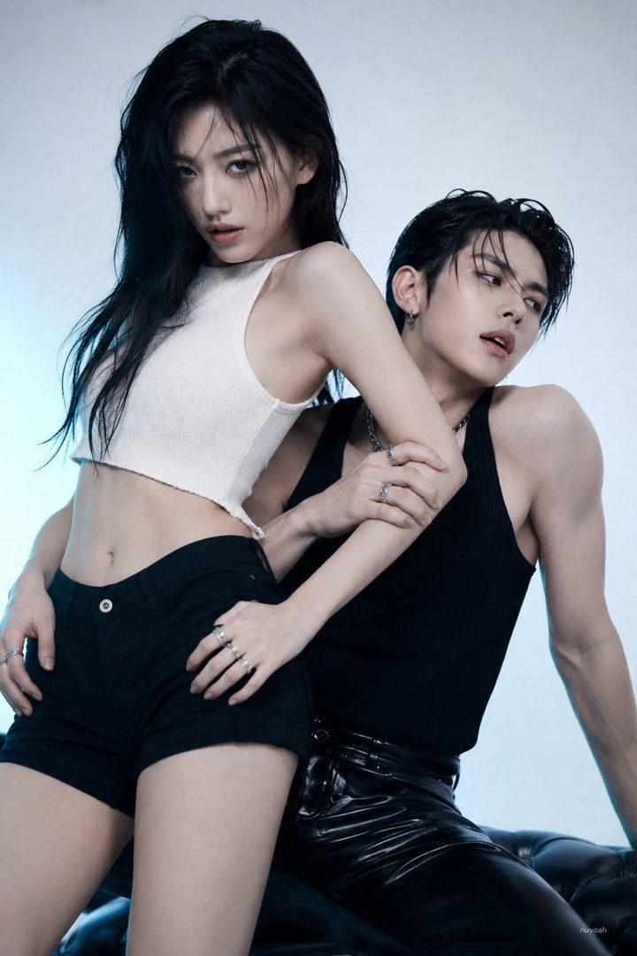 A man and a woman with black hair pose together in a studio, both wearing casual dark clothing and looking cool.