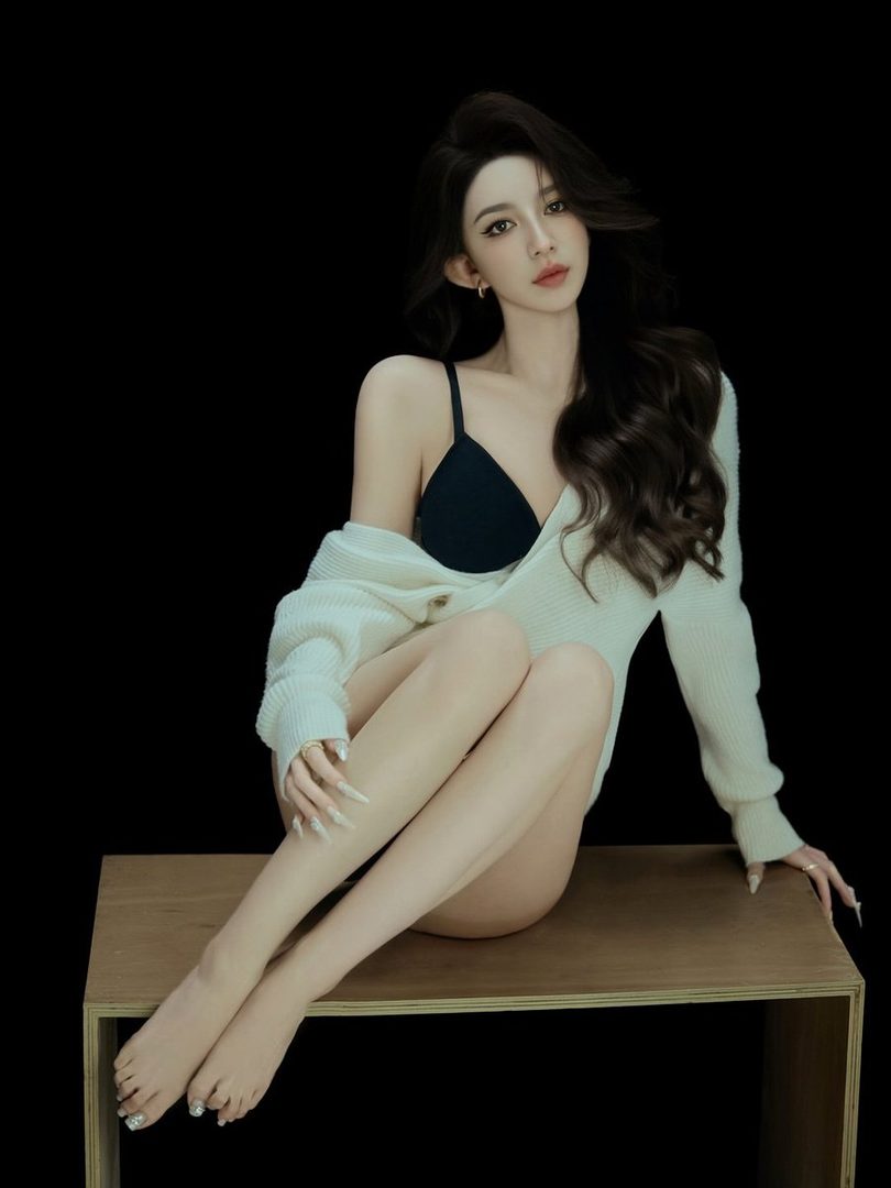A photorealistic portrait of a woman with long brown hair, wearing a black bra and an off-the-shoulder white knit sweater, sitting on a wooden bench against a black background.