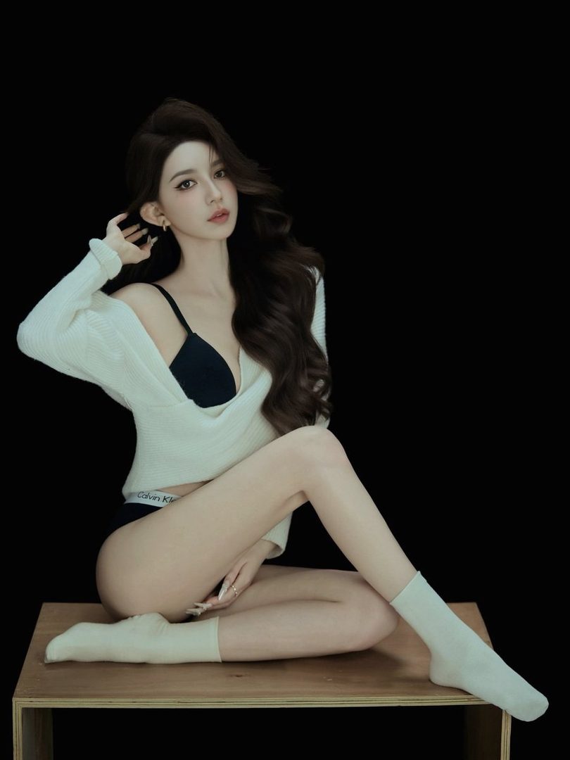 A photorealistic portrait of a woman with long brown hair, wearing a white knit top and black underwear, sitting on a wooden surface against a black background.