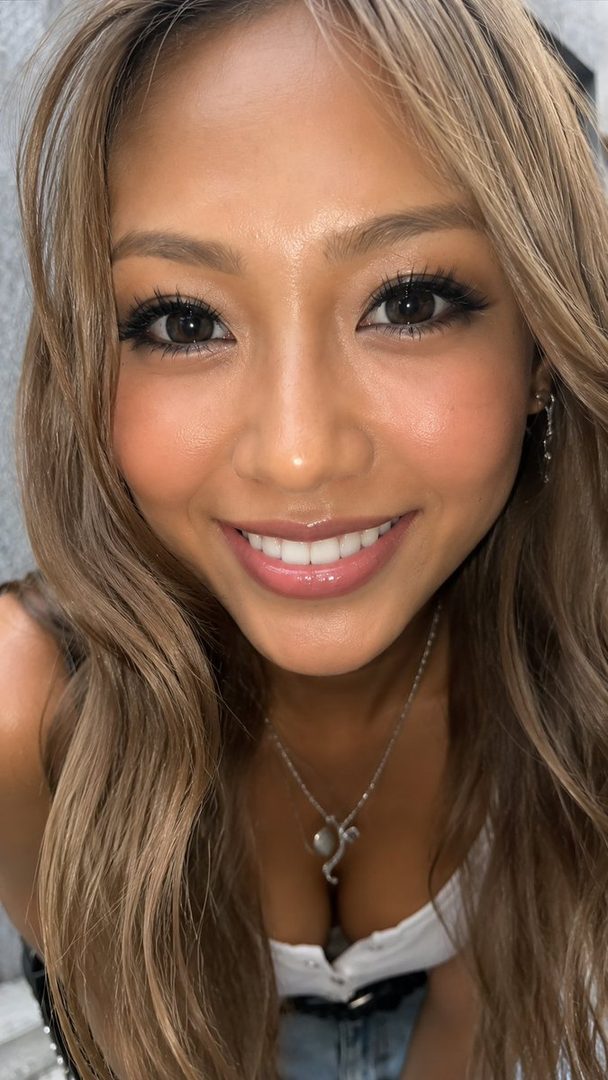 A close-up portrait of a smiling woman with long blonde hair and a low-cut top, looking directly at the camera.