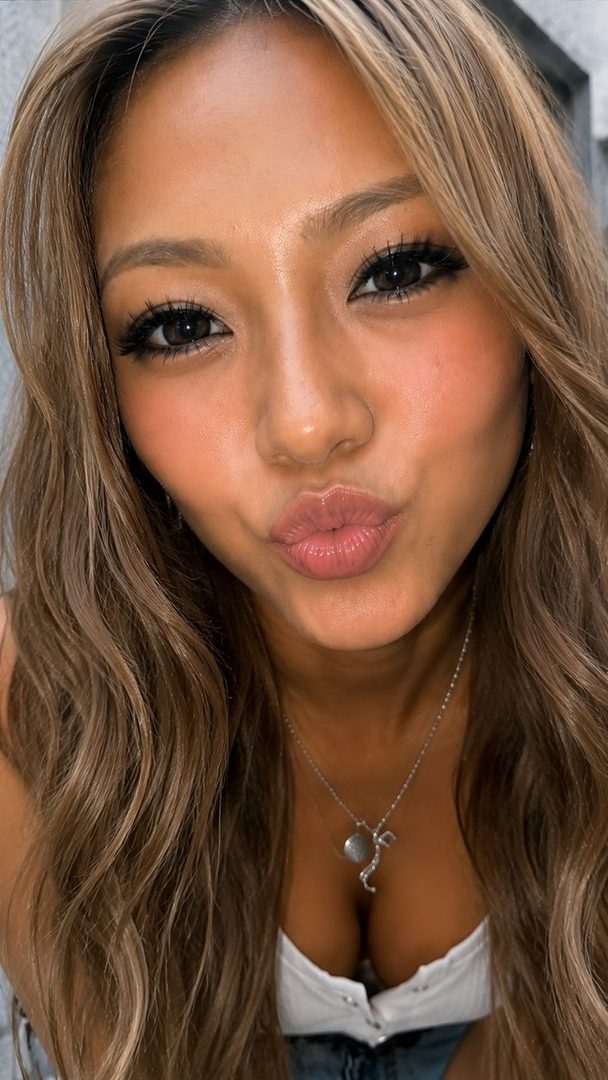 A close-up portrait of a woman with long blonde hair, making a kissy face.