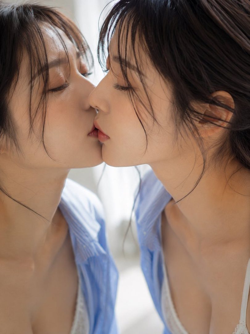 A photorealistic portrait of a woman kissing her reflection, with her eyes closed and wearing a blue shirt.