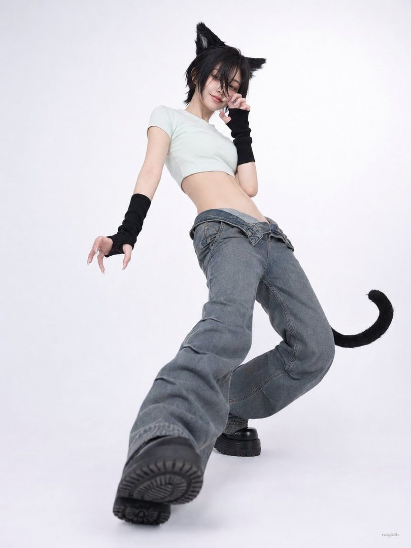 A playful woman with short black hair and cat ears poses in a studio, wearing a light green crop top, baggy jeans, and black arm warmers.