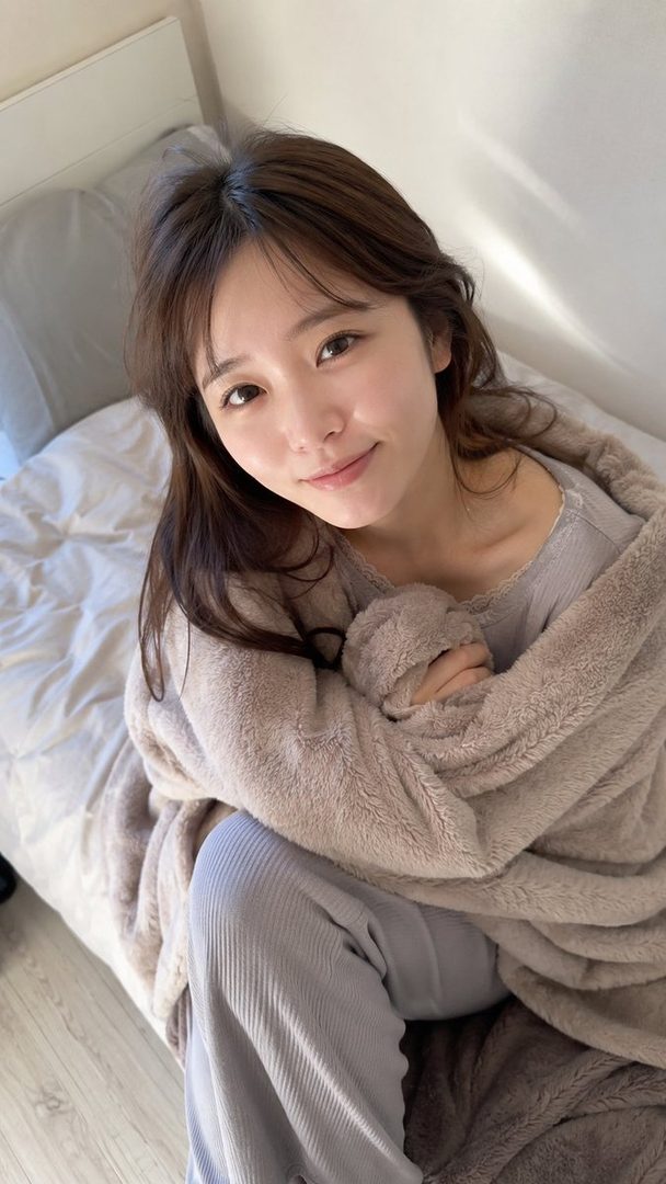 A young woman with brown hair is wrapped in a cozy blanket, looking directly at the camera with a gentle smile.