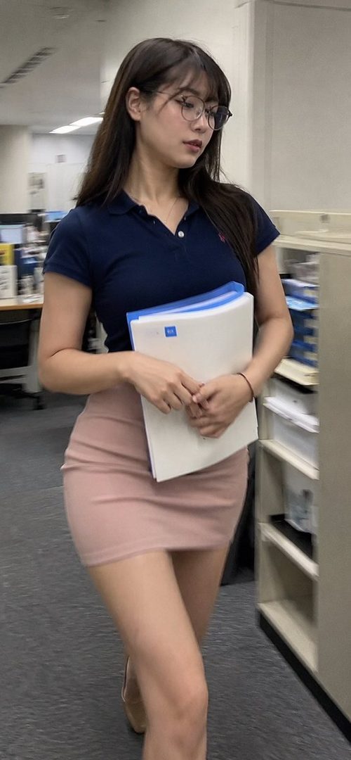 A young woman with long brown hair and glasses, wearing a navy polo shirt and a pink mini skirt, walks through an office holding documents.