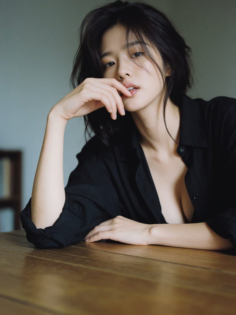A photorealistic portrait of an East Asian woman with short black hair, wearing an unbuttoned black blouse, resting her arm on a wooden table.