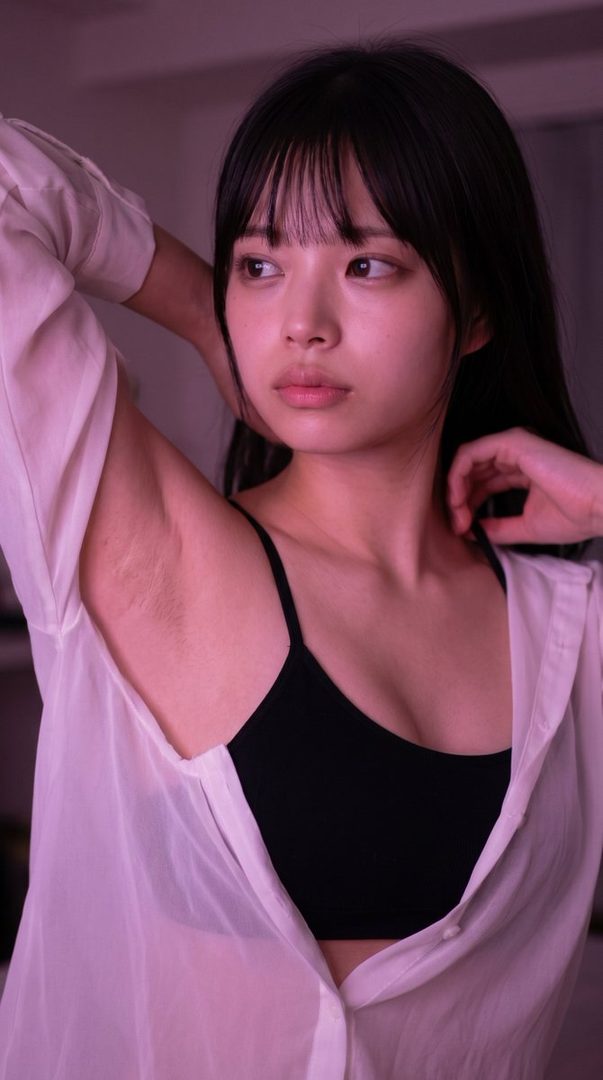 A young woman with black hair and bangs wears a black bra and an open white blouse, looking away with a dreamy expression.