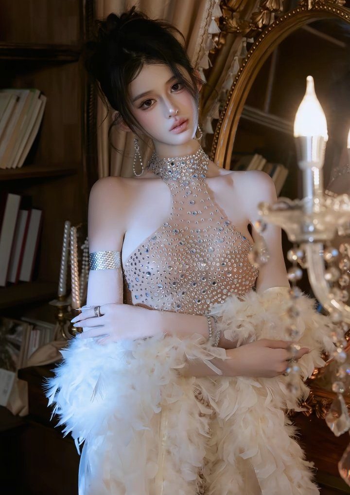 A woman with dark hair in an elegant, jeweled dress with a feather boa, posing indoors.