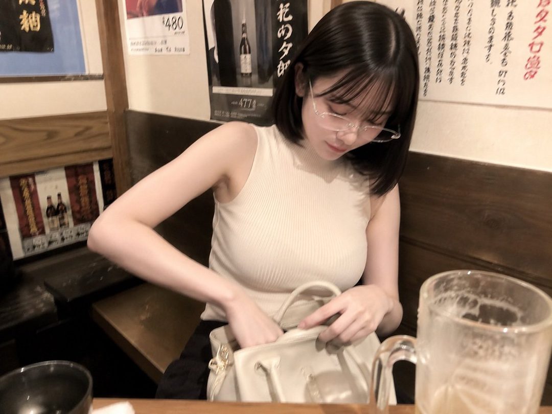 A young woman with short black hair and glasses is seen indoors, looking into her bag.