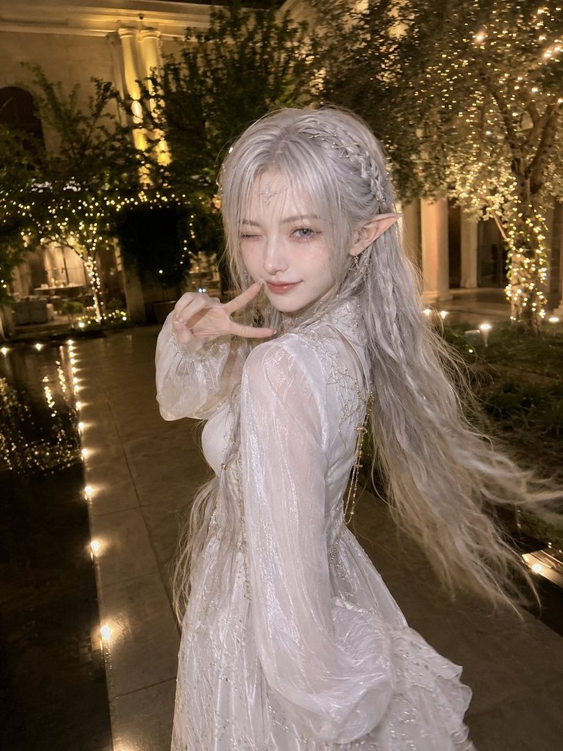 A beautiful elf-like woman with long silver hair and a white dress winks at the camera in a magical outdoor setting at night.