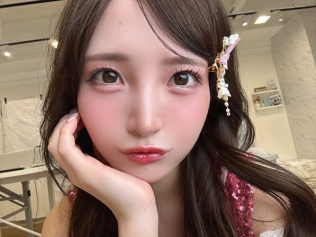 A close-up portrait of a woman with long brown hair, wearing a pink sequined top and a decorative hair clip, looking directly at the camera.