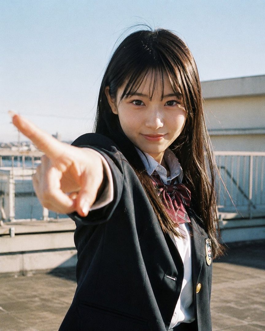 A young woman in a Japanese school uniform points directly at the viewer from a rooftop.