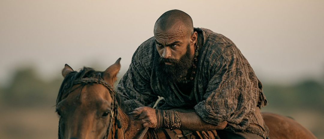 A photorealistic portrait of a bald man with a long beard, wearing a rustic tunic, riding a horse in an outdoor setting.