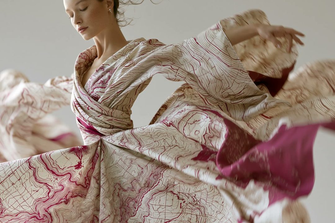 A high-fashion editorial portrait of a woman wearing an avant-garde dress made from flowing topographic maps, featuring muted and bold contrasts.