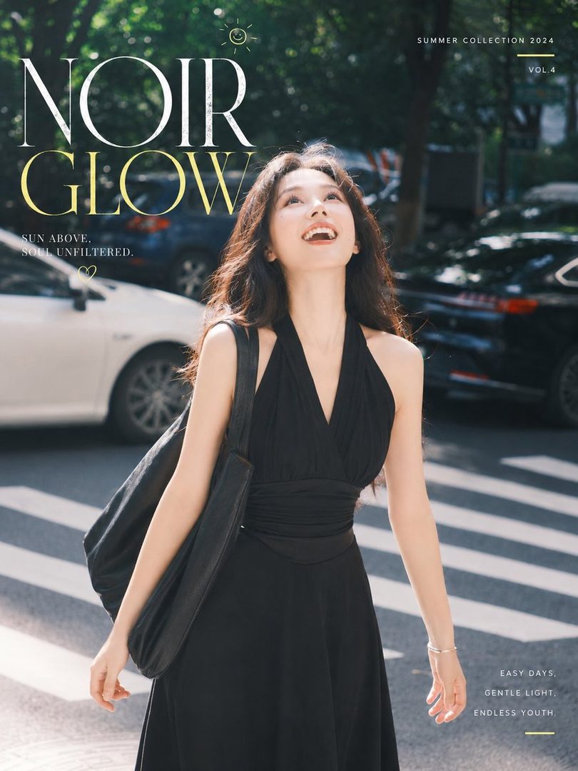 A young woman in a black halter dress smiles and looks up while walking on a sunny street.