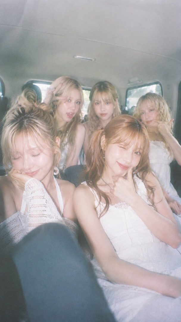 Five young women with blonde and brown hair are sitting in a car, smiling and posing for the camera.
