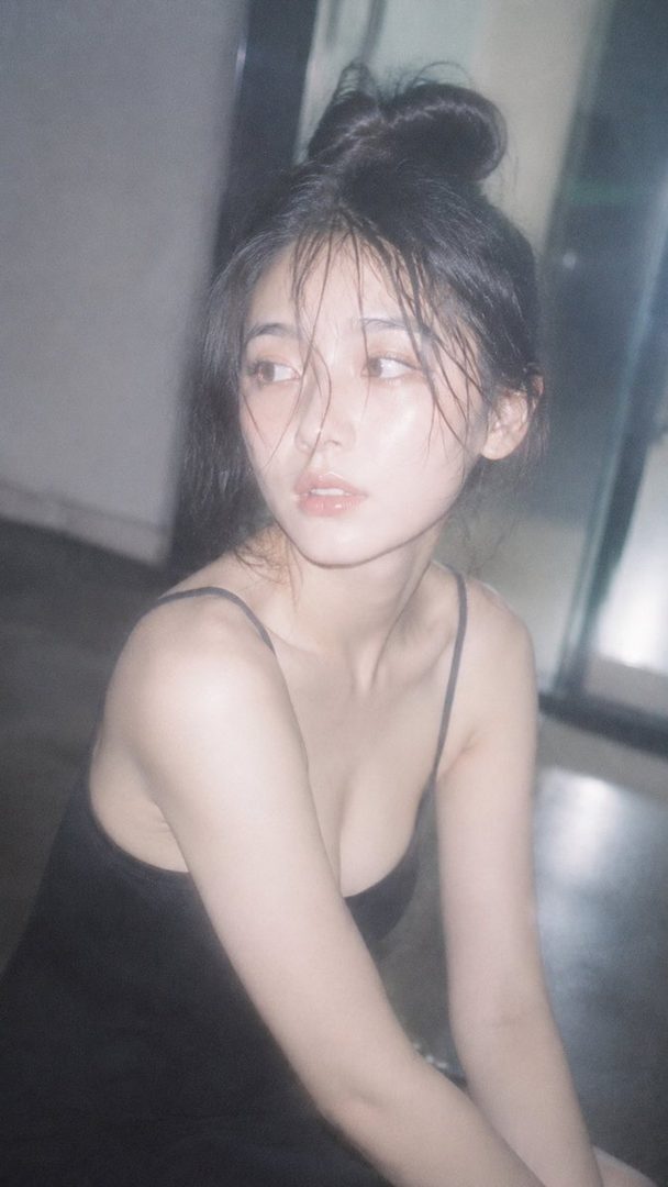 A photorealistic portrait of an East Asian woman with black hair tied up, wearing a black camisole, looking away with a dreamy expression.
