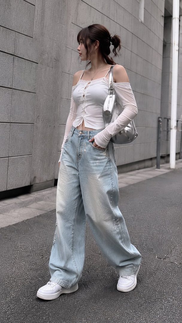 A young woman with brown hair tied in a ponytail, wearing a white off-shoulder top and light blue baggy jeans, walks down a city street.