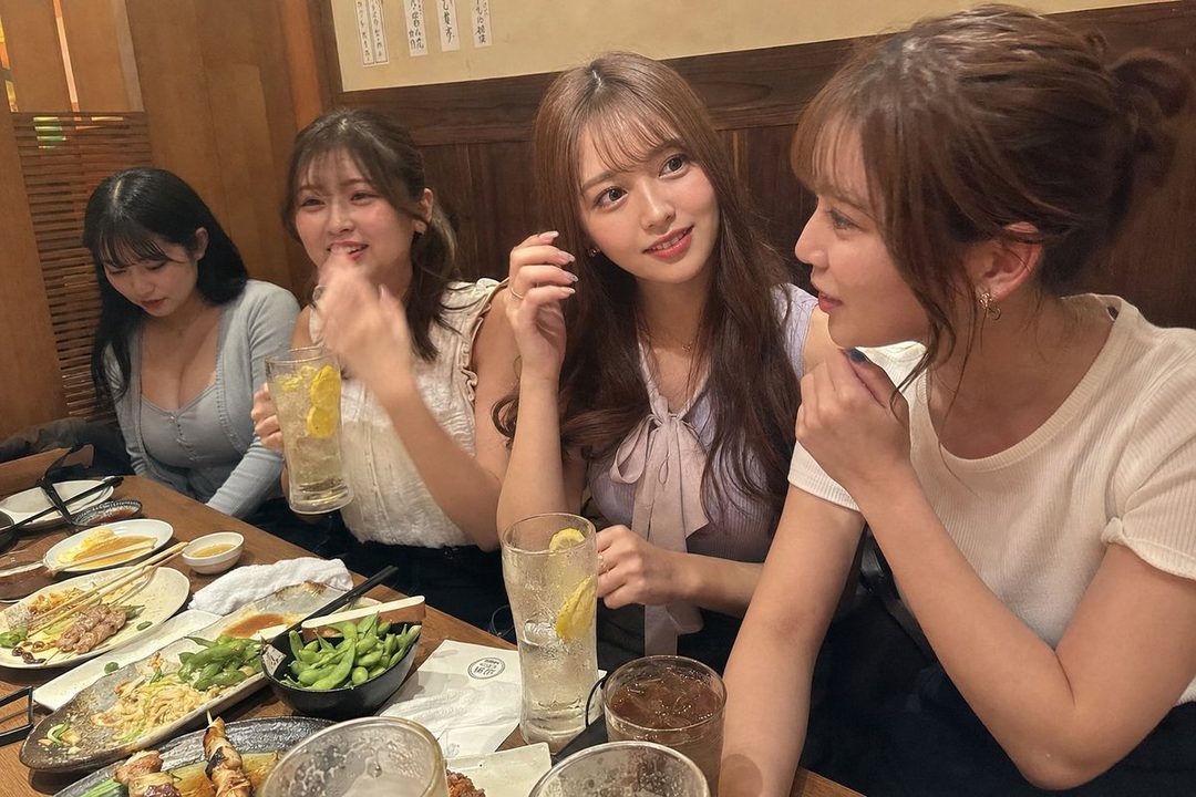 Four young women are sitting at a table in a restaurant, enjoying drinks and food.