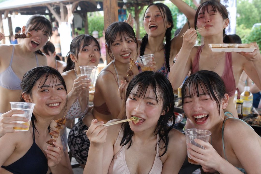 A group of young Japanese women in swimwear are enjoying food and drinks outdoors on a hot summer day.