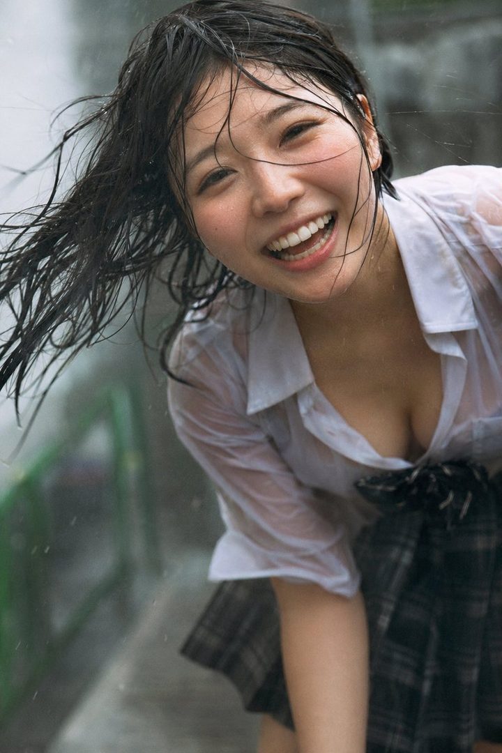 A young woman with wet black hair and a white shirt smiles brightly in the rain.