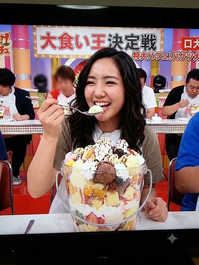A young woman with long black hair smiles while eating a giant parfait from a bucket, with other people in the background.