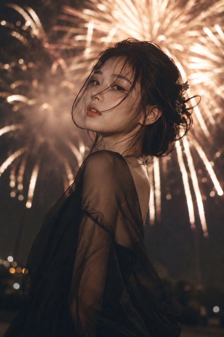 A beautiful woman with dark hair looks over her shoulder against a backdrop of bright fireworks at night.