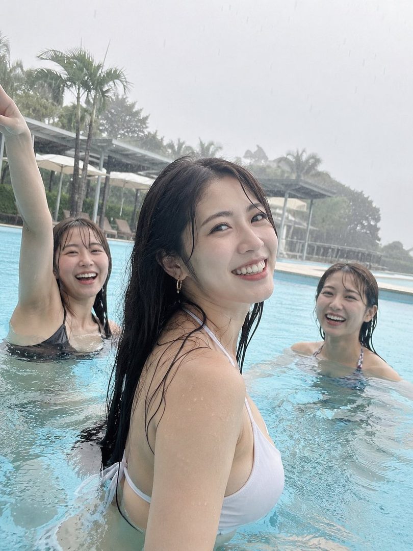 Three young women are smiling and playing in a swimming pool on a rainy day.