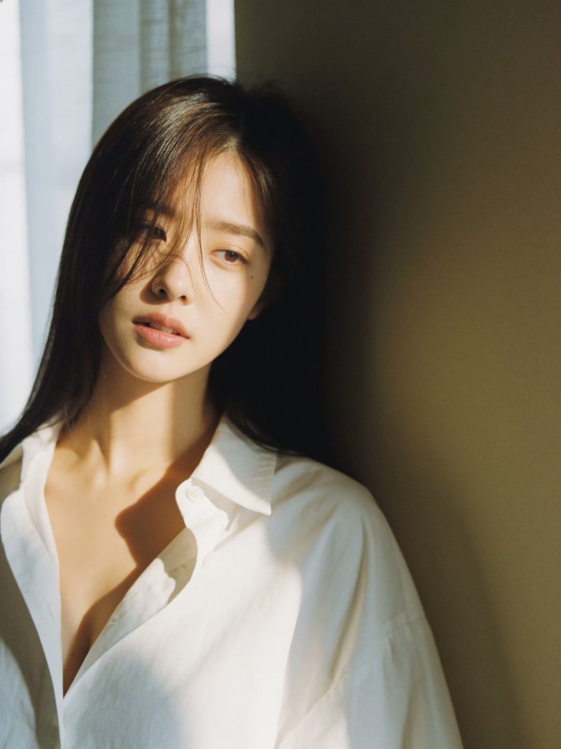 A photorealistic portrait of a young East Asian woman with long dark hair, wearing a white collared shirt, bathed in soft sunlight indoors.