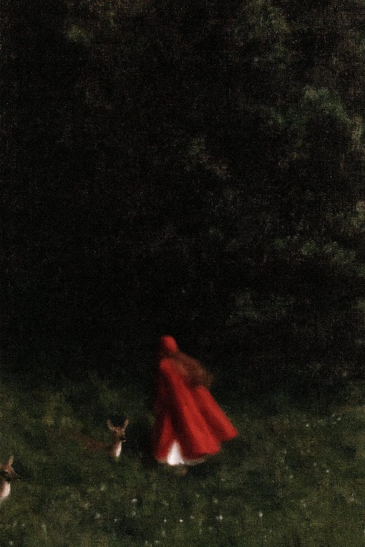 A person in a red cloak walks through a grassy field with deer, evoking a fairy tale scene.