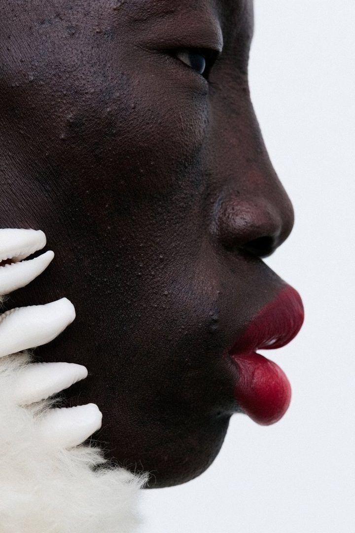 Close-up profile portrait of a dark-skinned person with striking red lipstick and white fluffy accessory.