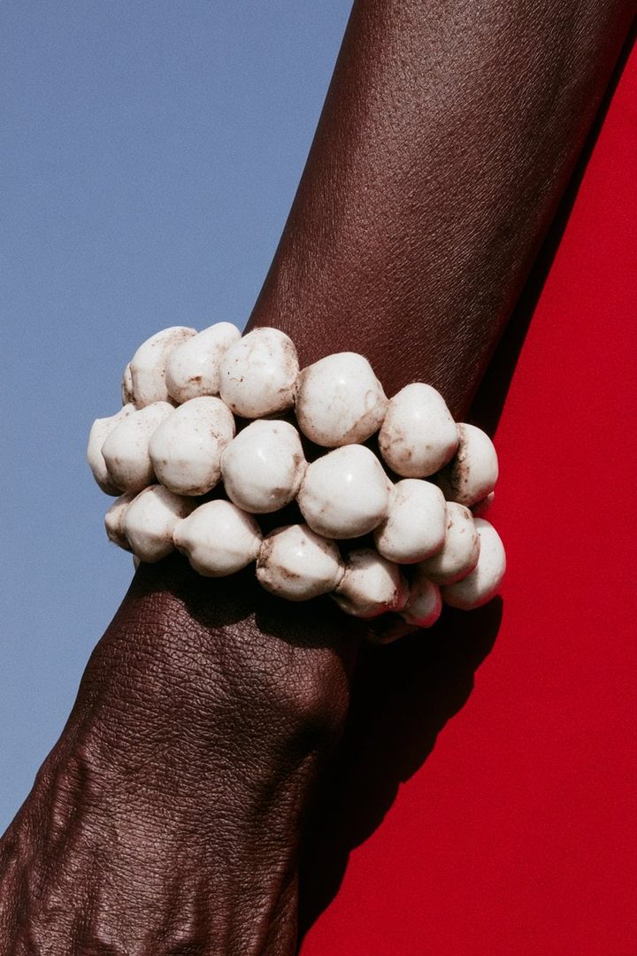 Close-up of a person's arm wearing a bracelet made of white beads against a blue and red background.