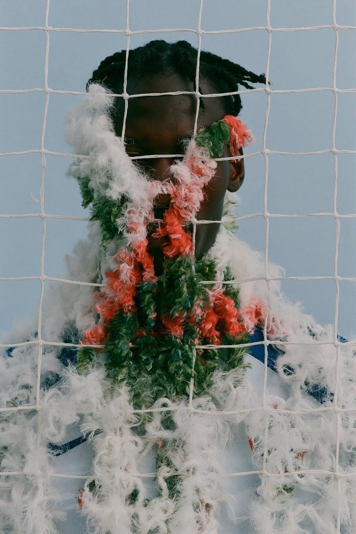 A portrait of a person wearing a fluffy, colorful scarf and a net in front of them.
