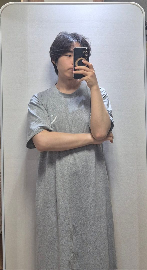 A person takes a selfie in a mirror, wearing a grey t-shirt and with short black hair.