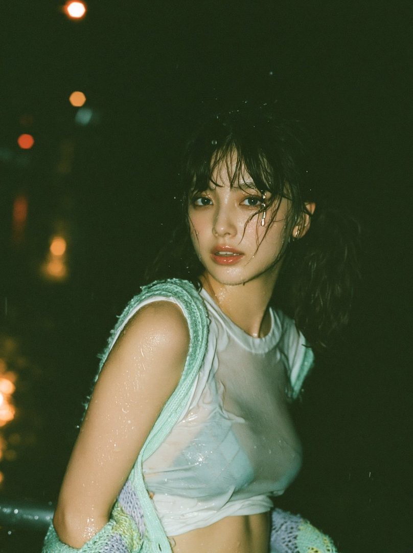 A wet young woman with pigtails looks out from the darkness, her white t-shirt clinging to her body.