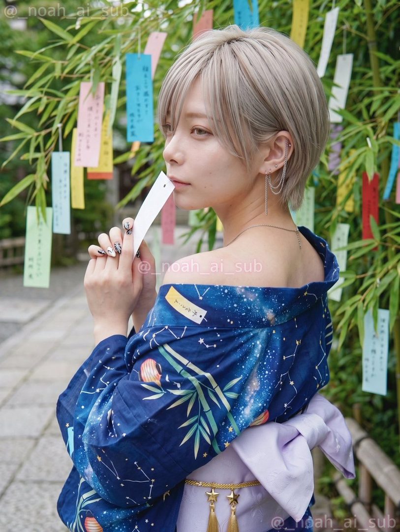 A young woman with short blonde hair wearing a blue yukata with a starry night pattern, holding a white paper strip, standing outdoors near a bamboo tree with colorful tanzaku papers.