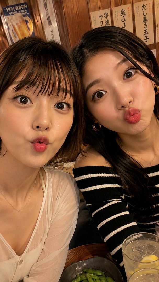 Two young East Asian women making duck faces at the camera in a restaurant setting.