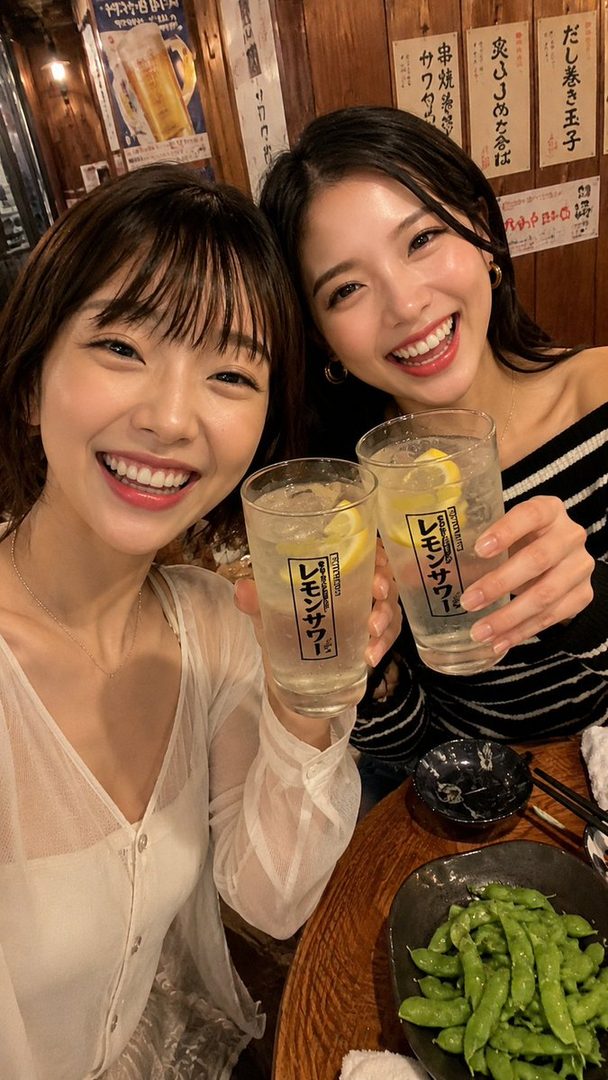 Two young Japanese women smiling and holding drinks in a bar, taking a selfie.