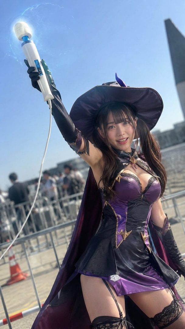 A young woman in a witch costume, holding a magic wand, poses outdoors with a smile.