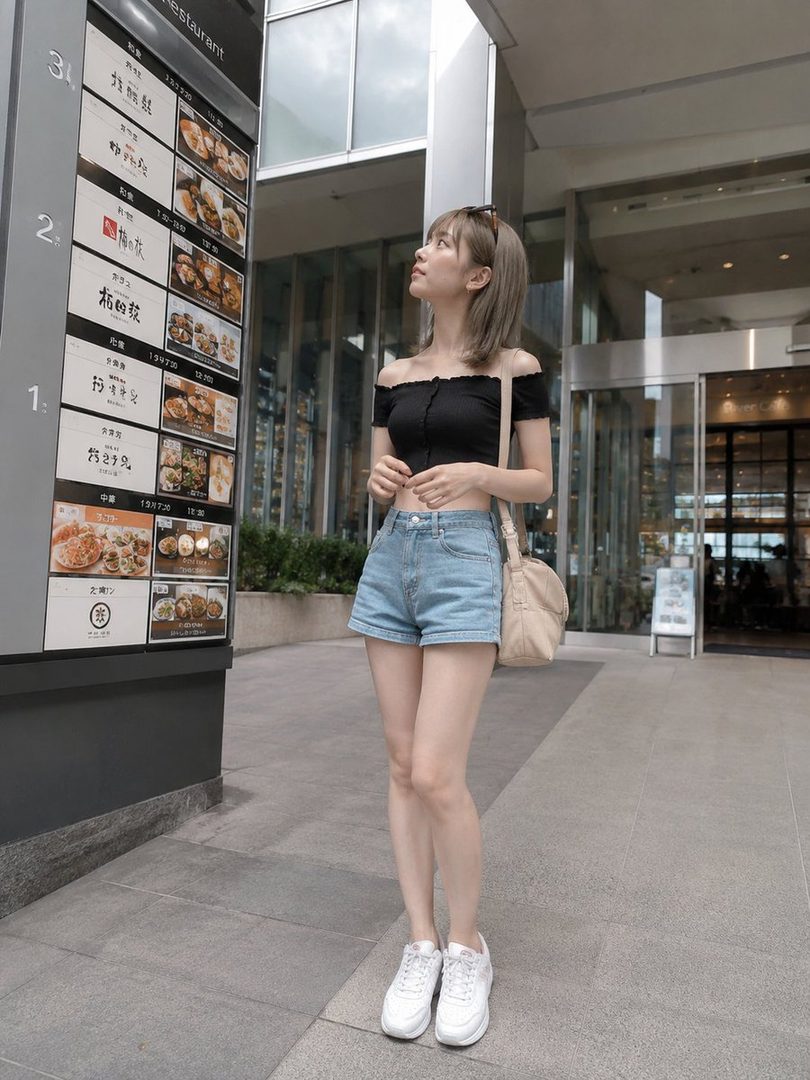 A young woman in a black off-the-shoulder top and denim shorts stands outside a restaurant, looking up at a menu.