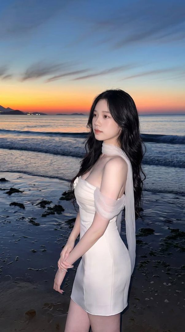 Photorealistic portrait of a beautiful young East Asian woman in a white dress on a beach at sunset.