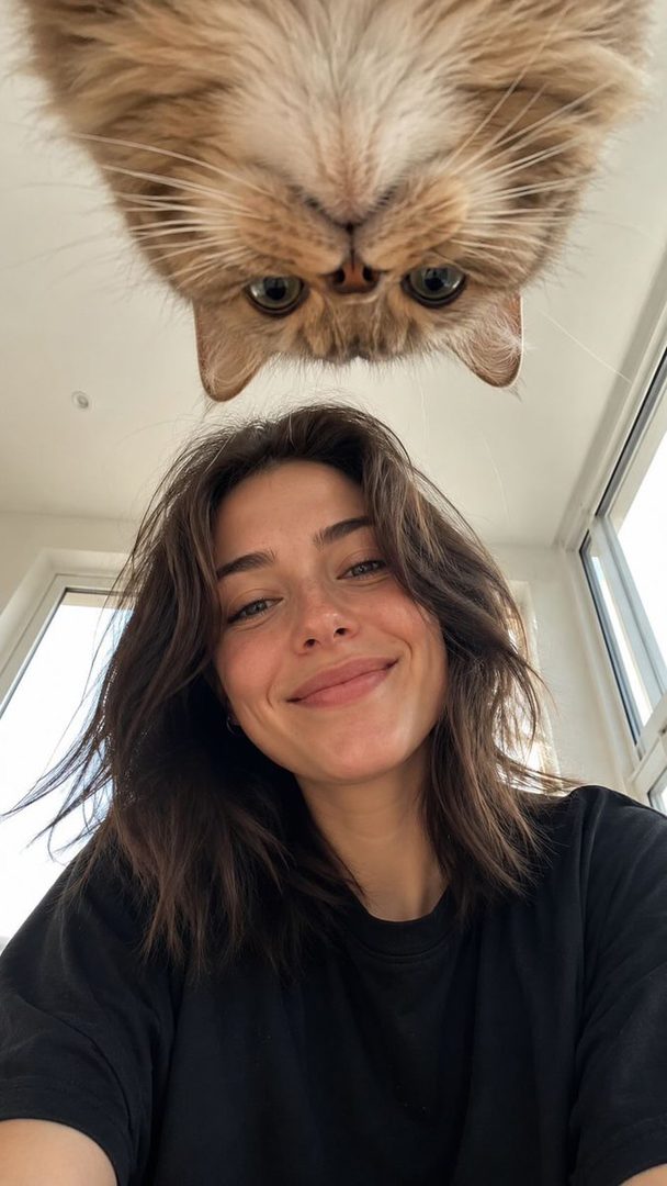 A woman takes a selfie with her fluffy cat looking down from above.