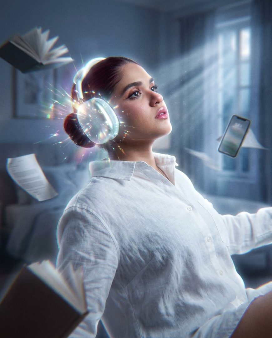 A young woman with headphones on, looking up as books and a phone float around her in a surreal bedroom setting.