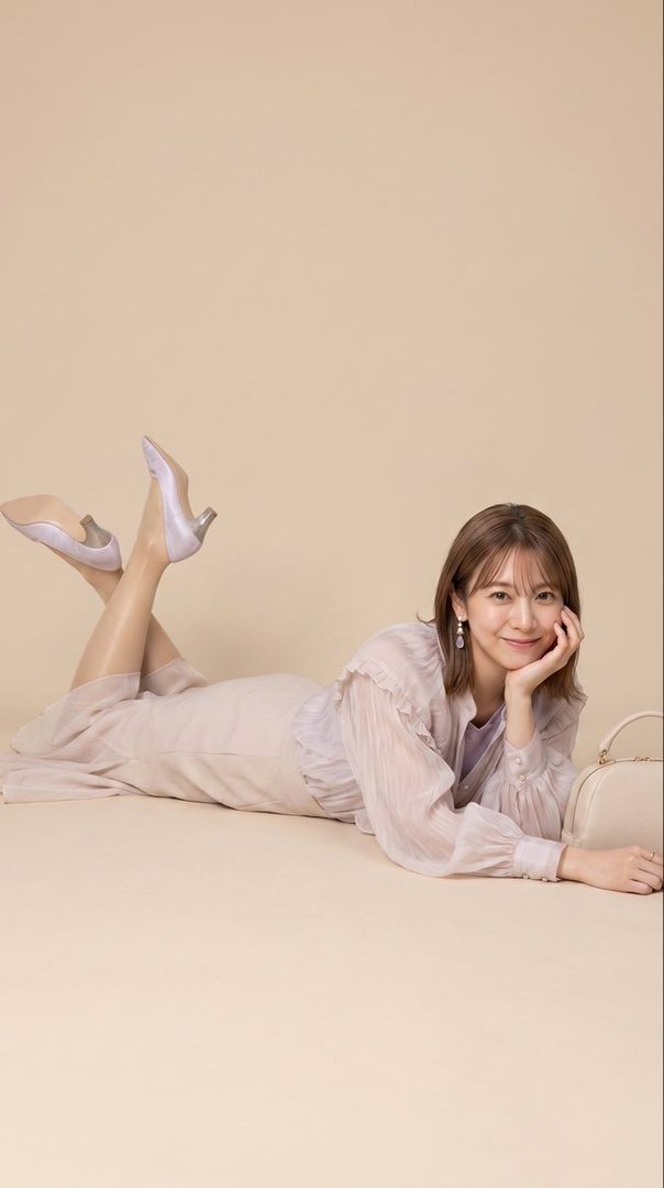 A woman with shoulder-length brown hair, wearing a light purple dress and heels, poses lying down in a studio setting.