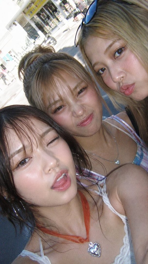 Three young East Asian women taking a selfie outdoors on a sunny day, with playful expressions.